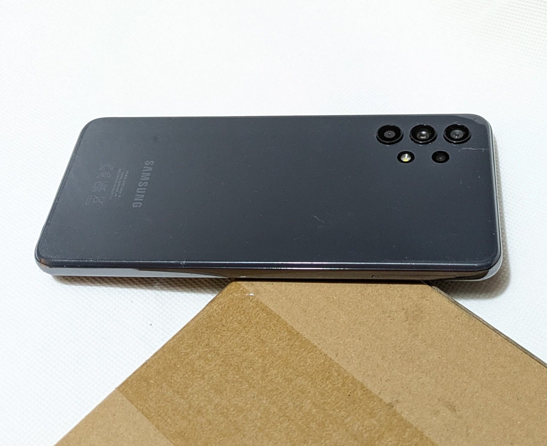 A refurbished Samsung Galaxy A32 smartphone placed on a cardboard surface, displaying its sleek black design, vertically aligned quad-camera setup, and the Samsung logo. Ideal for showcasing maintenance tips to keep refurbished devices performing like new.