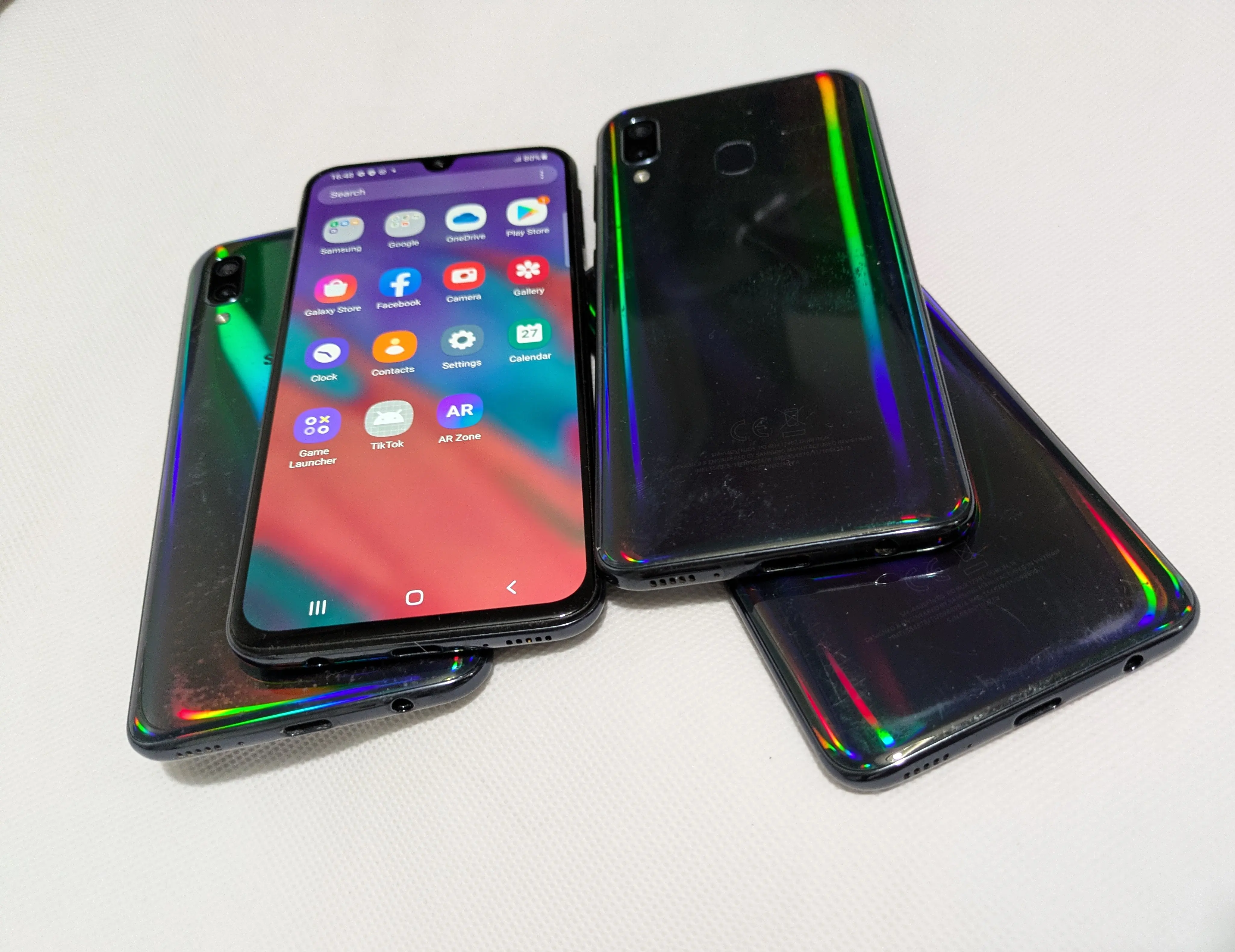 Four Samsung Galaxy A40 smartphones, three with their backs facing up and one with the screen facing up, displaying various app icons.
