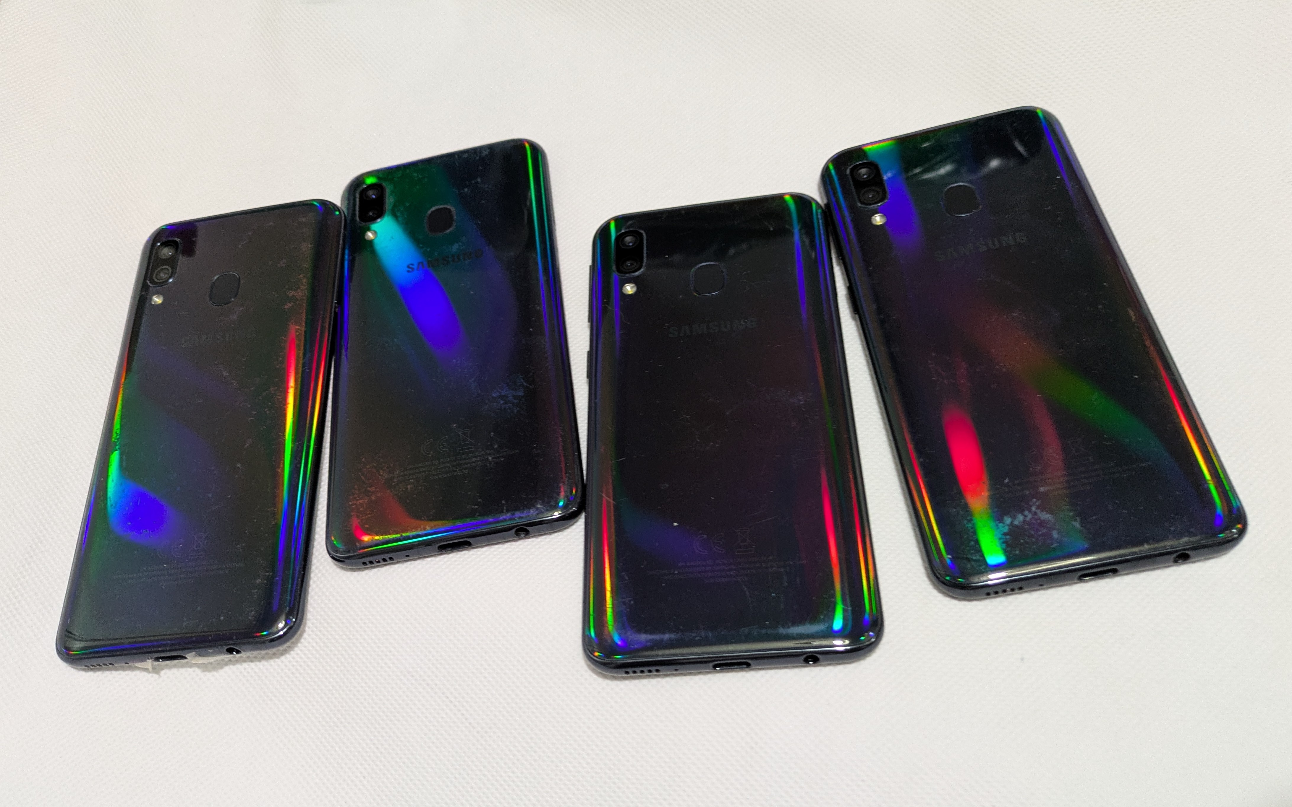 Four Samsung Galaxy smartphones placed on a white surface with a reflective, glossy back and a rainbow-like pattern due to light reflection, used phones for sale in liverpool
