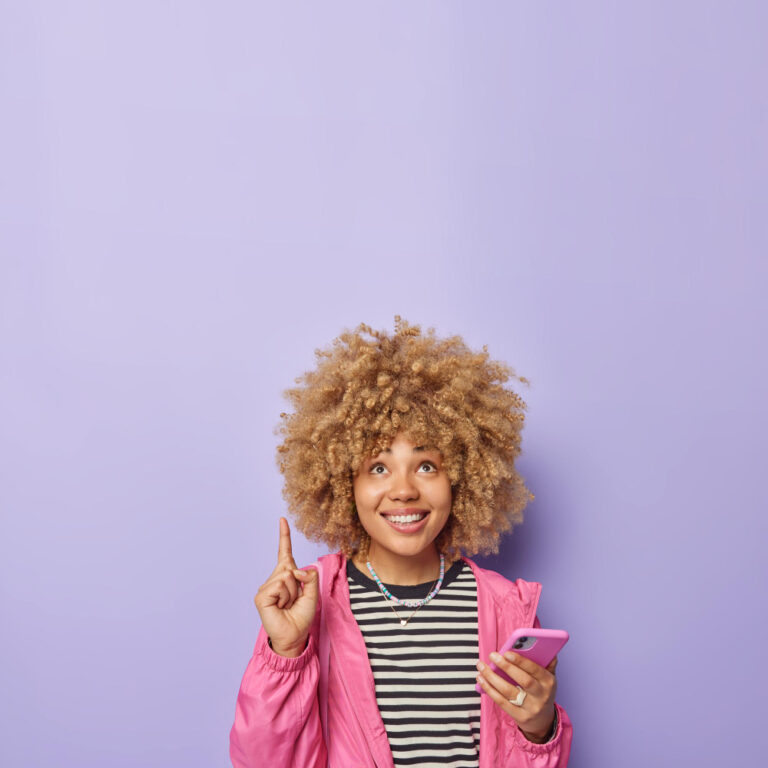 Person smiling and pointing upward while holding a smartphone, symbolising fun, social interaction, and positive energy.
