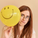 Woman smiling and holding a yellow balloon to represent emotional intelligence and personal growth